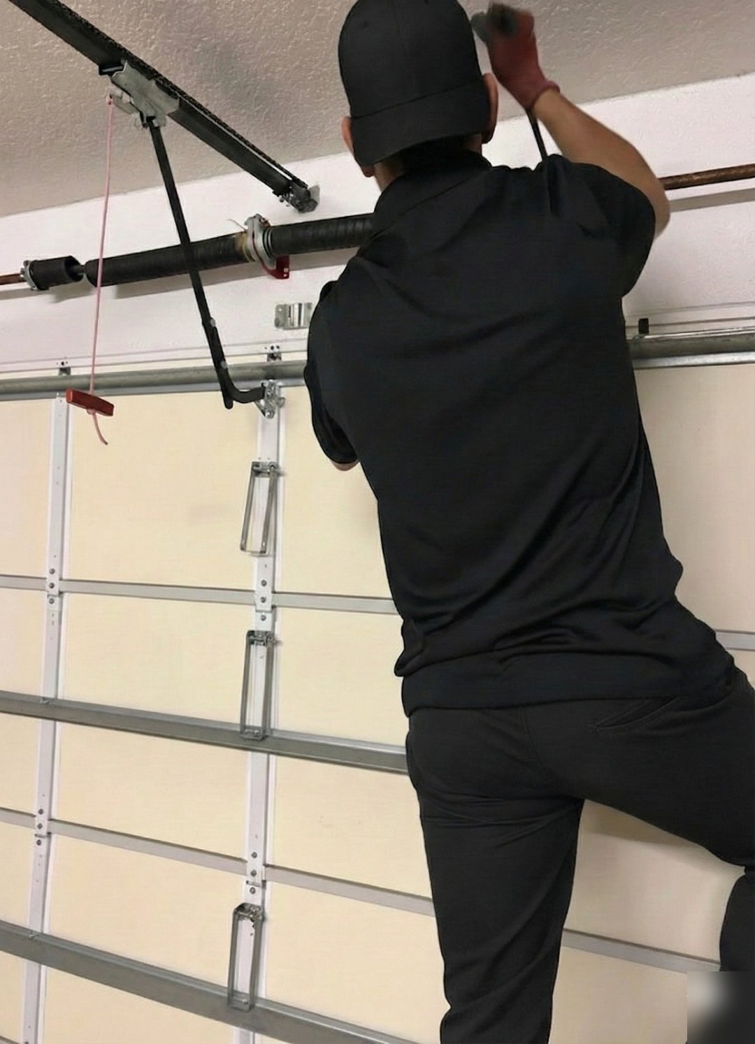Technician seen from behind reaching up toward spring hardware above a sectional door