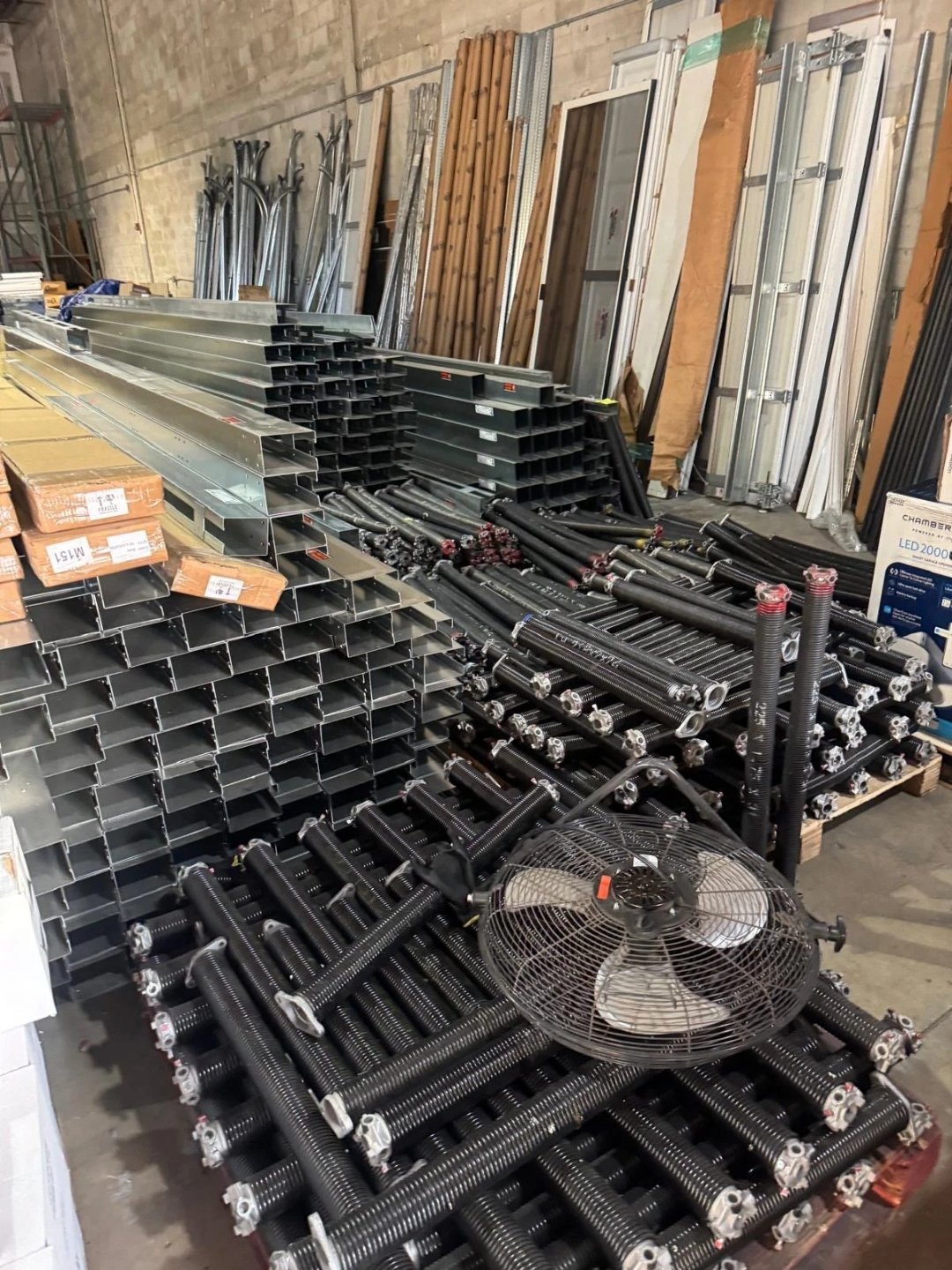 Stacked steel track sections and long spring assemblies beside a floor fan