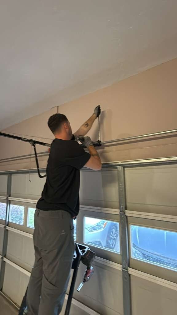 Technician on a stepladder adjusting hardware above a garage door with a row of windows