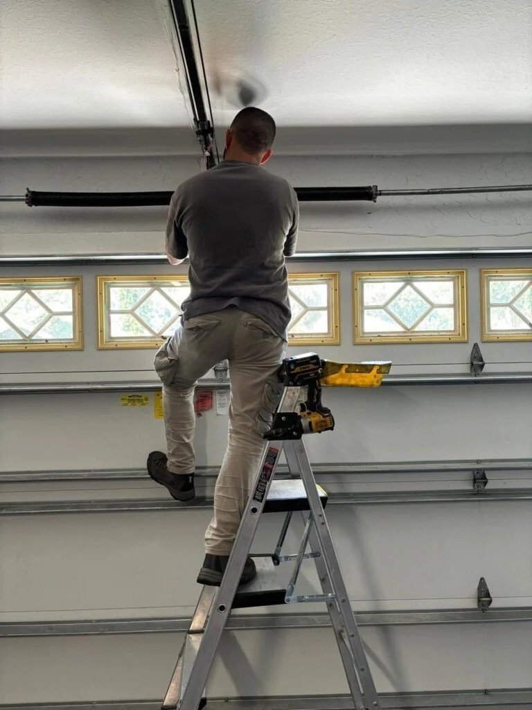 Technician on a stepladder using a cordless drill above a garage door with decorative window panels
