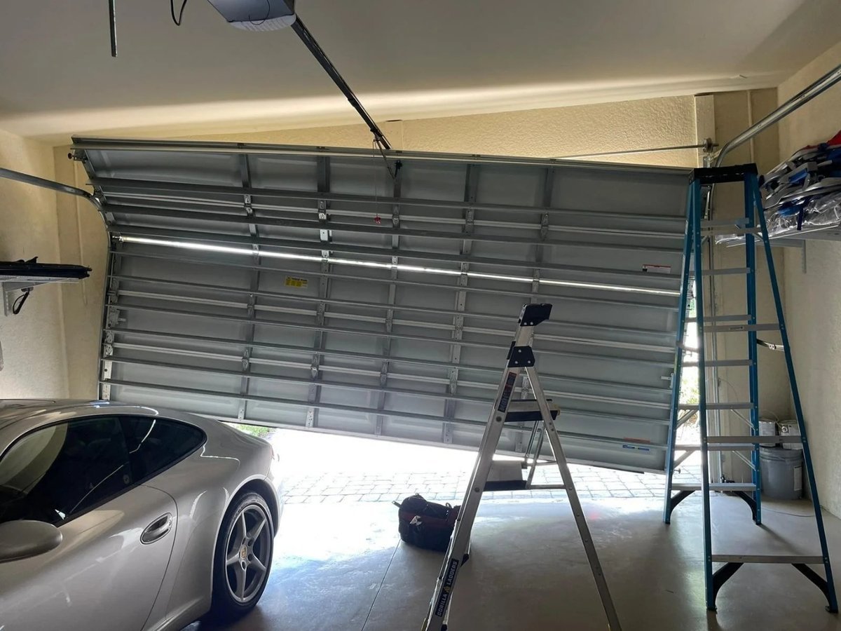 Partly raised metal garage door with two ladders and a car inside