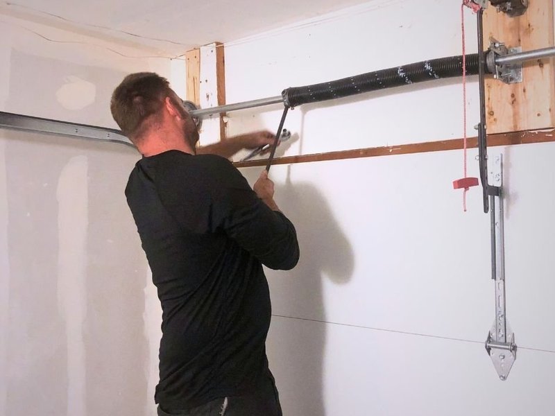 Technician reaching up to the spring hardware above a garage door